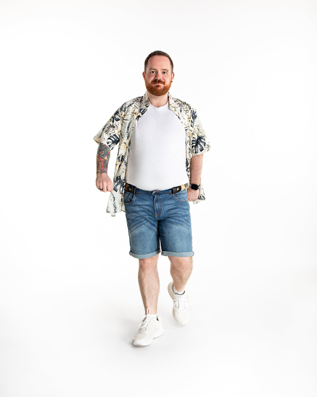 Man wearing a floral shirt, white t-shirt, denim shorts, and white sneakers on a white background.